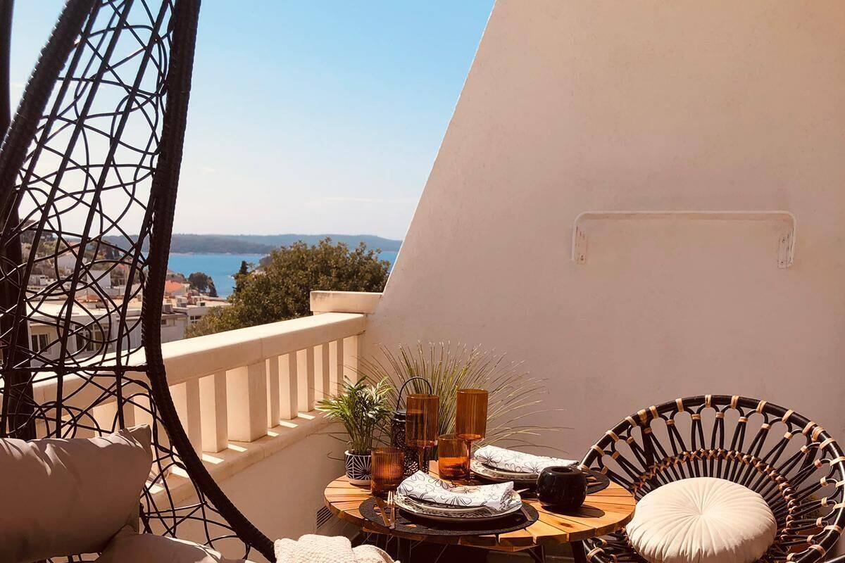 A balcony with wicker chairs, a small round table with a drink, and a view of the sea.