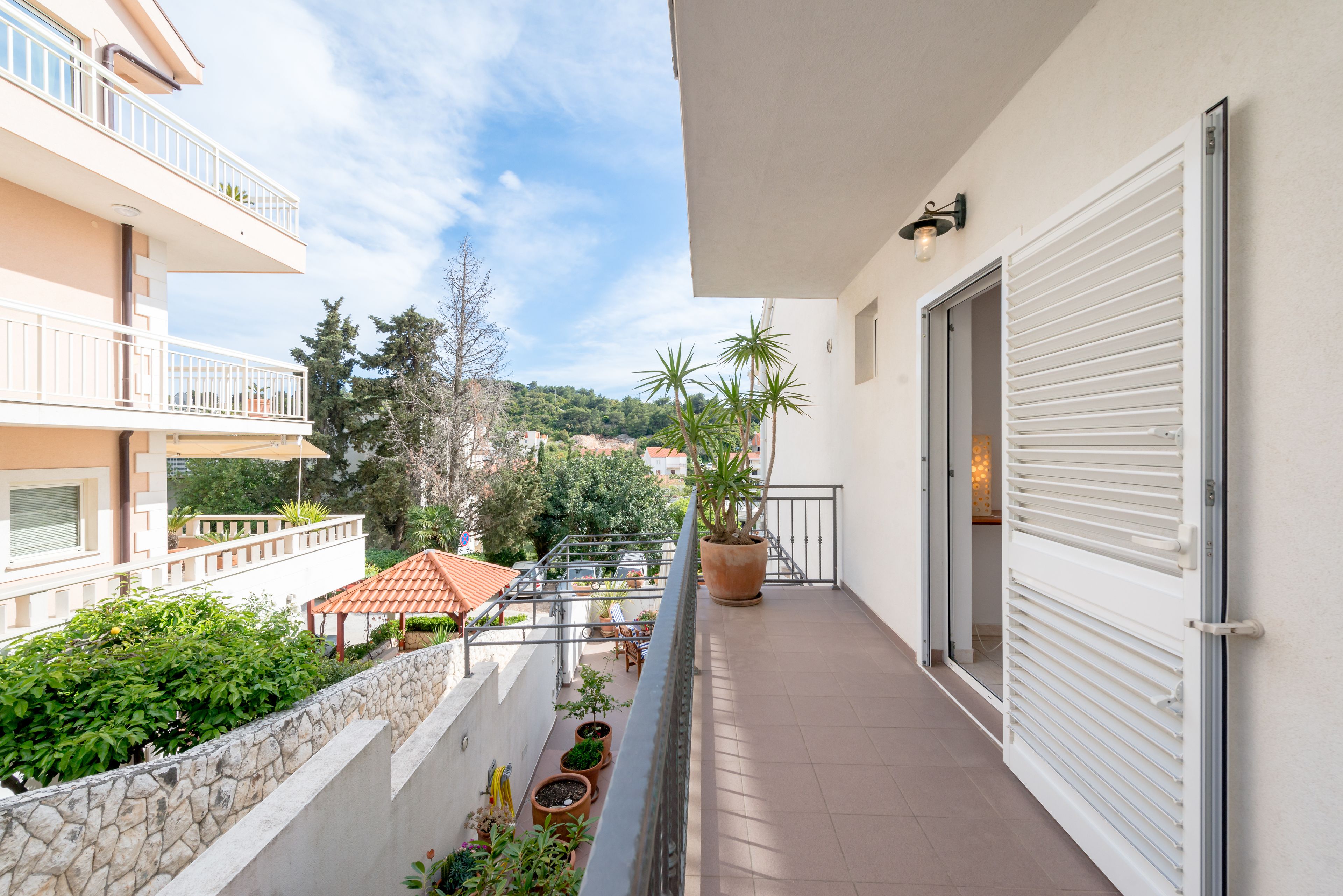 A balcony with potted plants, a stone wall, and a view of a hillside with buildings.
