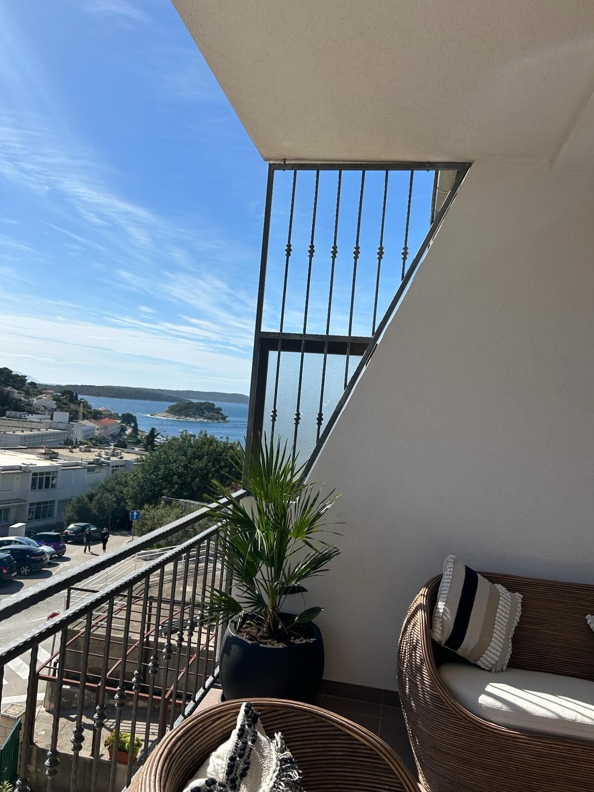 Uma varanda com vista para o mar, um vaso de planta e um sofá de vime.