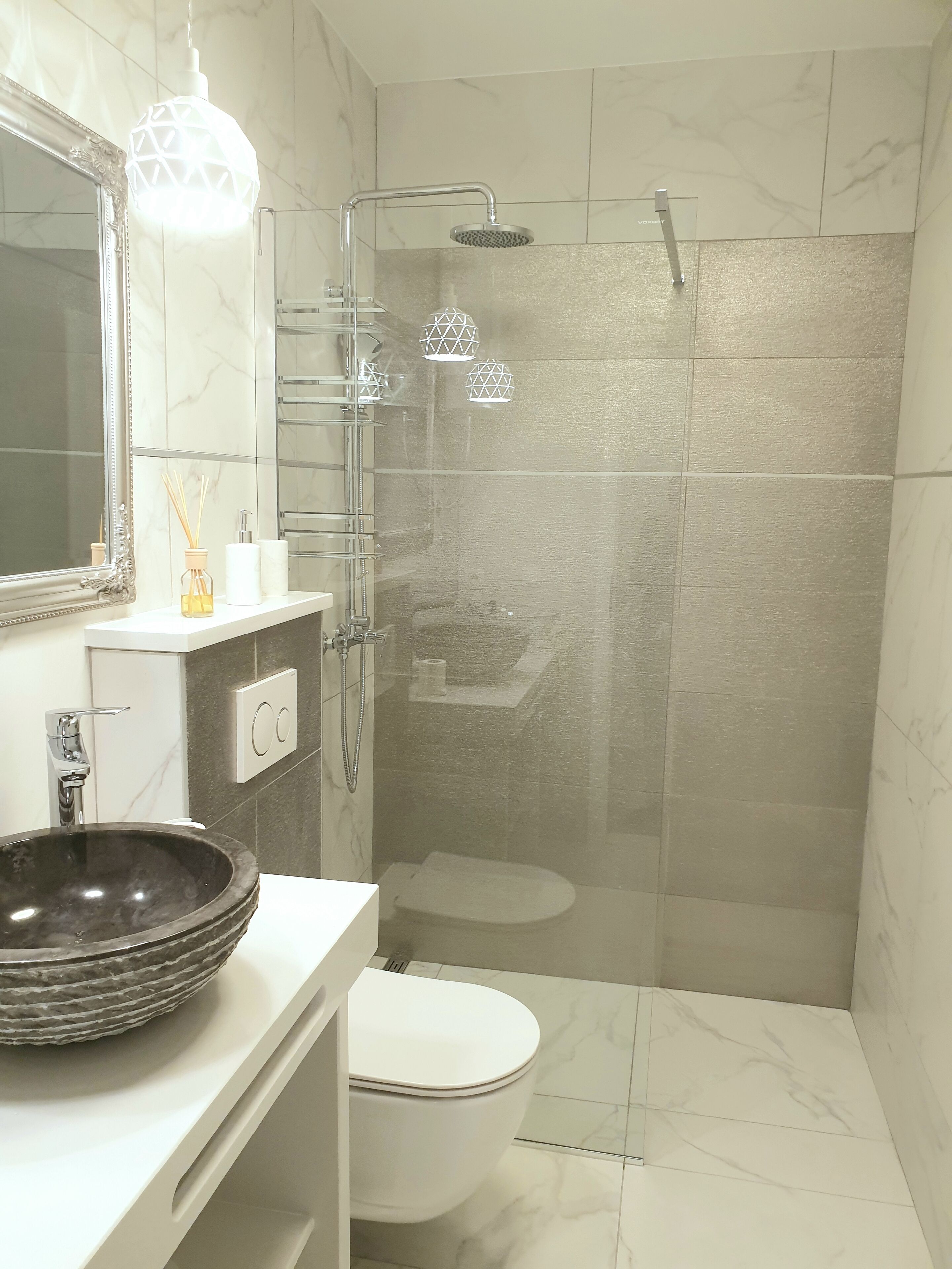 A modern bathroom with a large mirror, a round sink, a toilet, and a shower area.