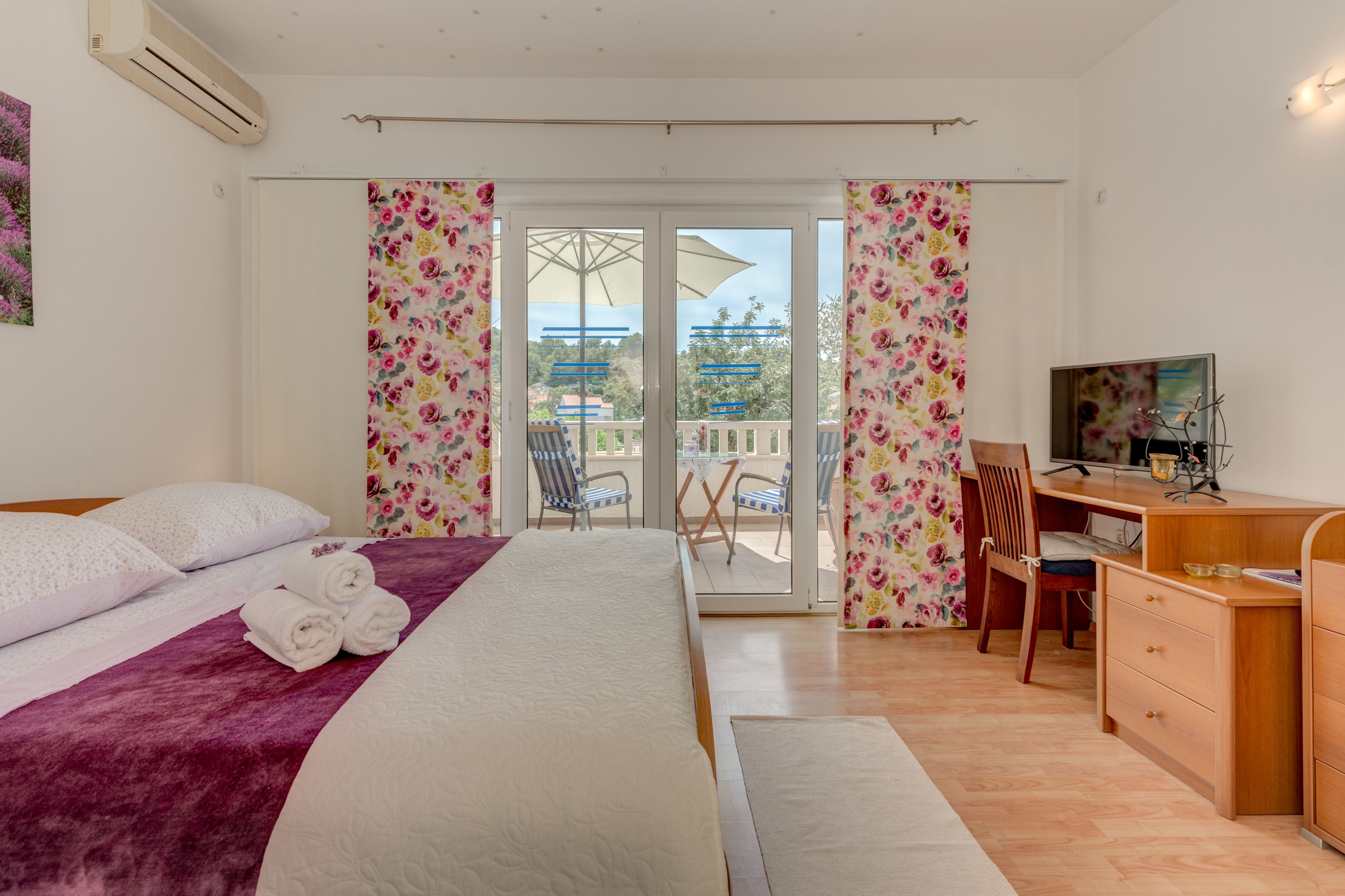 A bedroom with a bed, a desk, and a balcony with chairs.