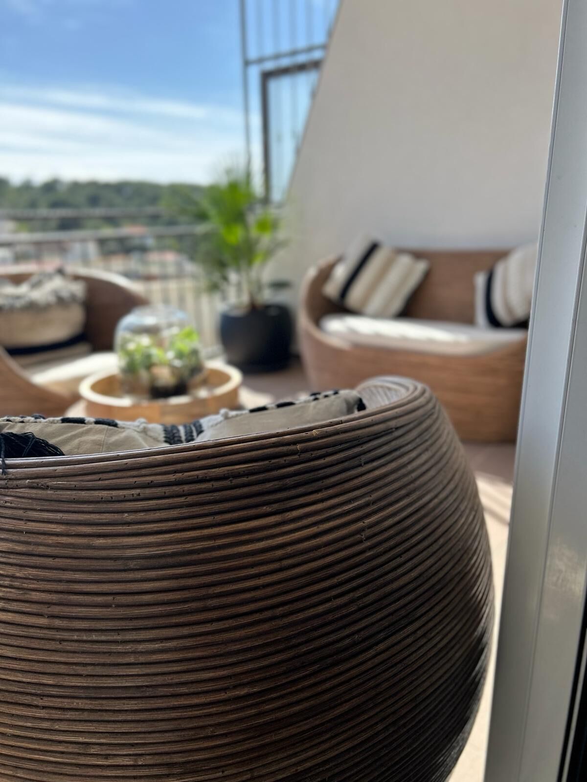 Una cesta de mimbre redonda y con textura sobre un balcón, con vistas al cielo y un paisaje lejano.