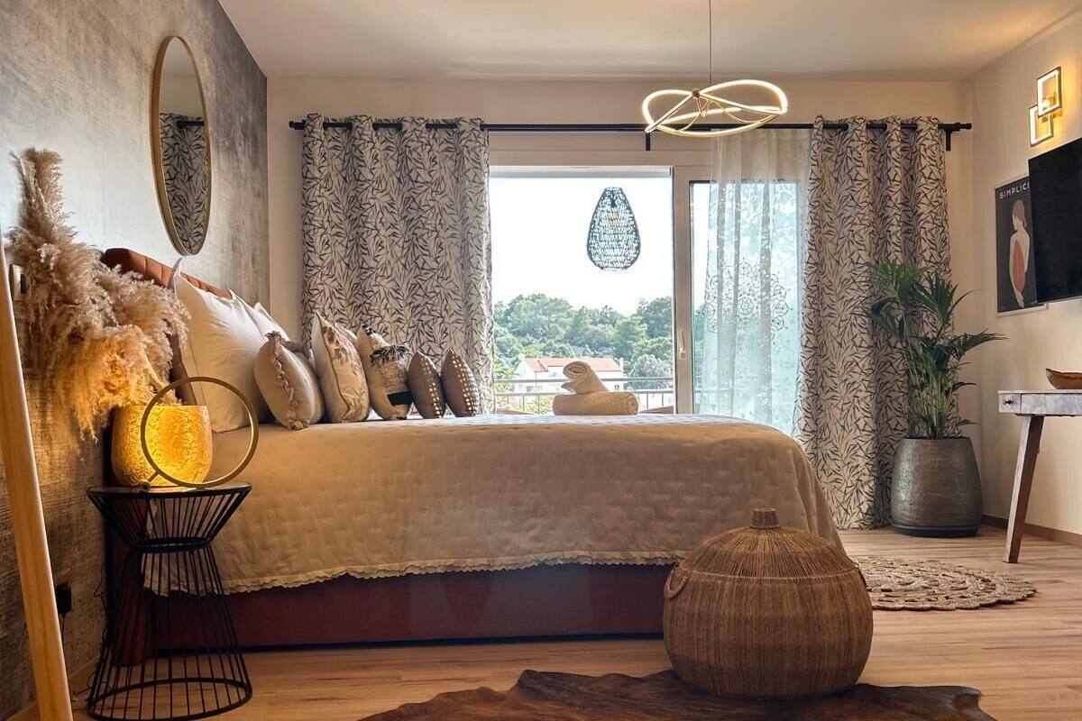 A modern bedroom with a large bed, a hanging light fixture, and a view of the outdoors.