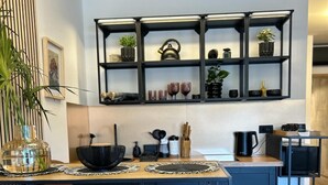 Una cocina moderna con una isla central, taburetes de bar, una pequeña mesa de comedor y una estantería empotrada sobre la encimera.