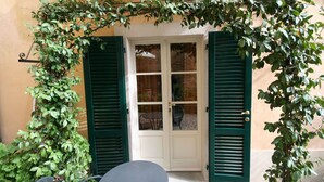 A doorway with green shutters, a glass door, and a small table with a chair in front. - Santo Agostino Belvedere - Apartment in Cortona (Cortona)