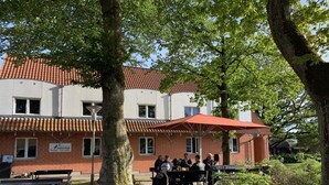 Une auberge de jeunesse avec un toit recouvert de tuiles rouges, un espace extérieur aménagé pour s’asseoir et une enseigne indiquant qu’il s’agit d’une auberge de jeunesse à Fjerreislø.