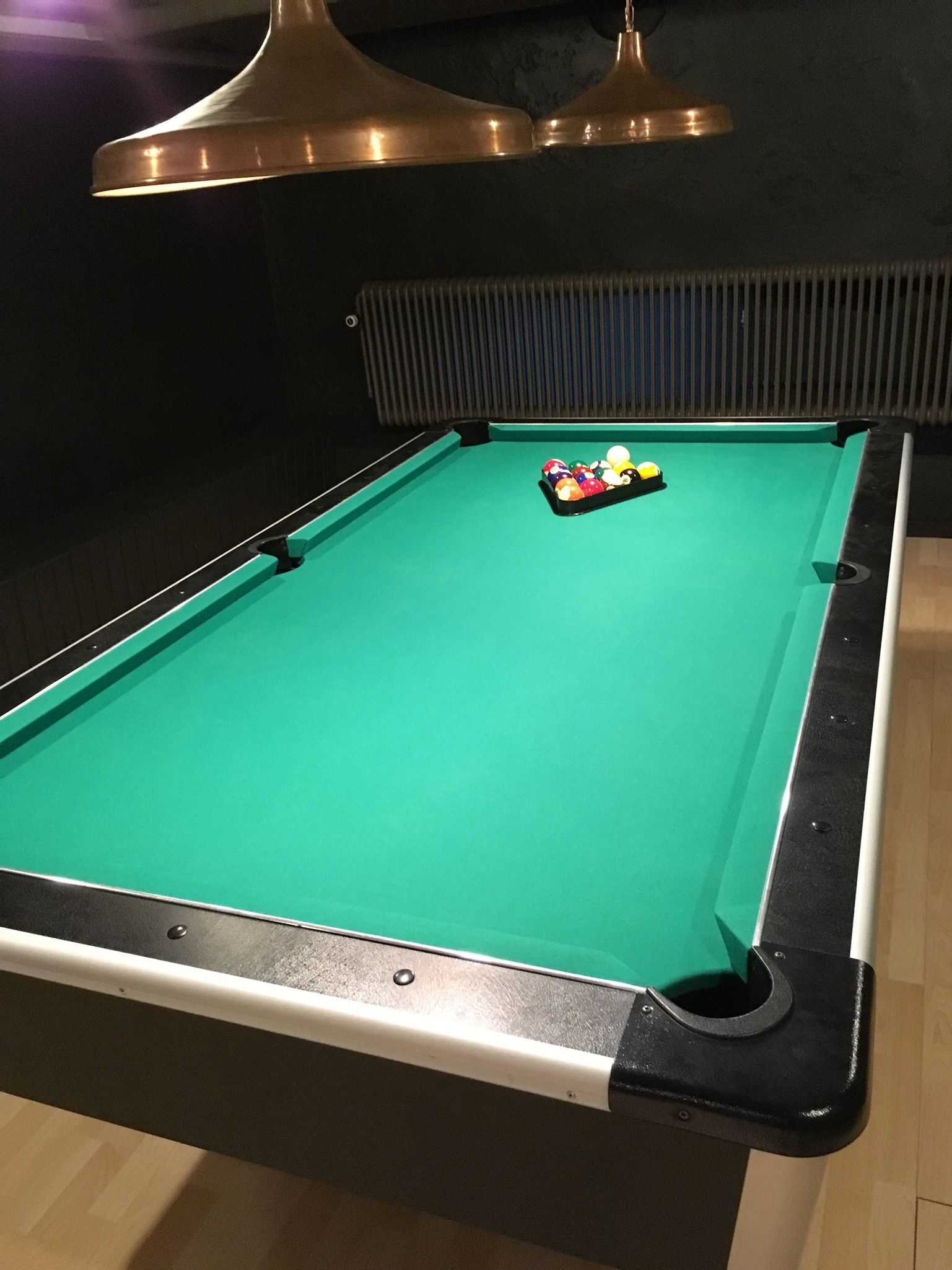 Una mesa de billar con superficie de fieltro verde, rodeada por un borde negro y un bolsillo negro en la esquina.