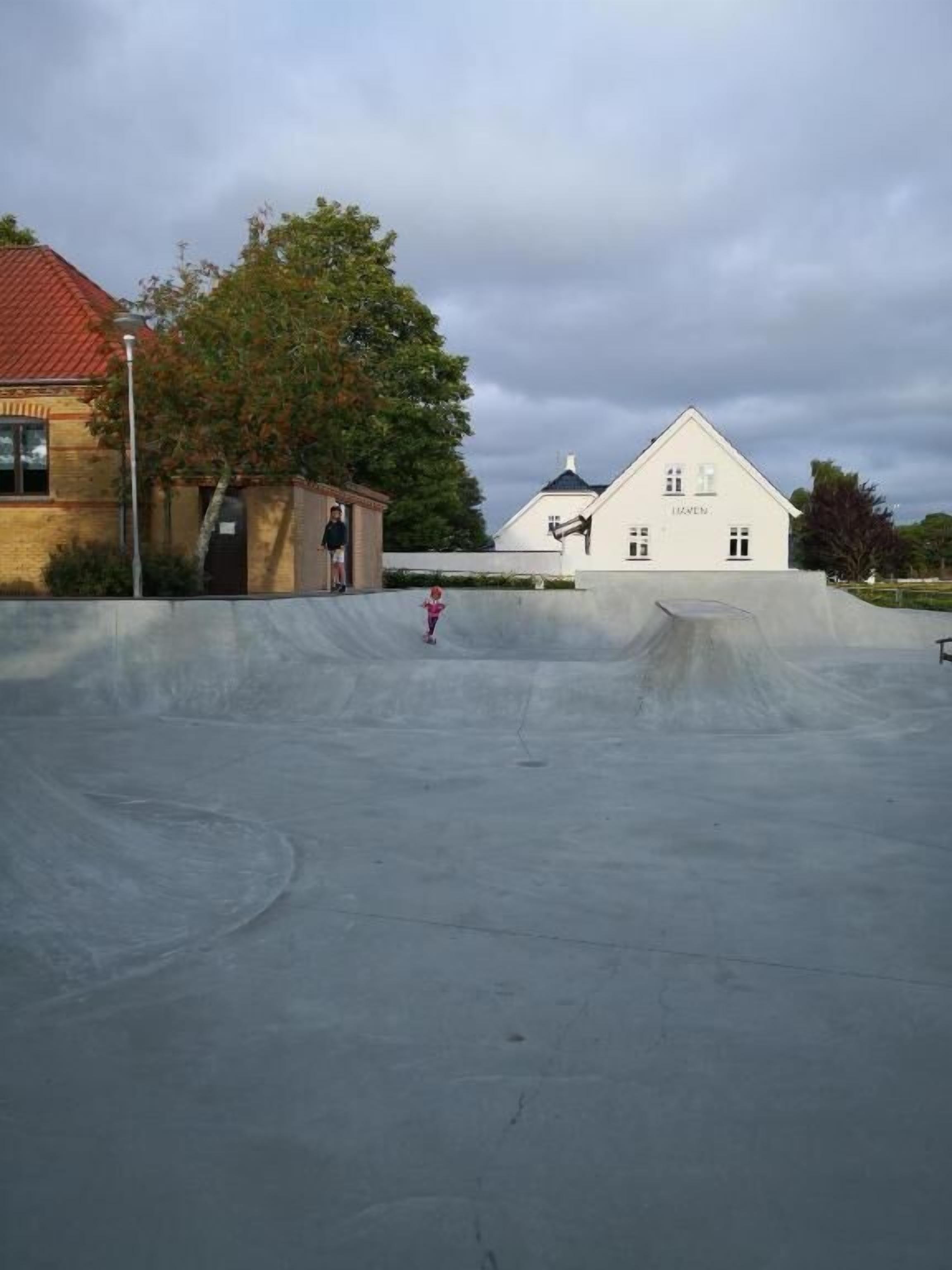 A skate park with a concrete ramp and a building in the background.