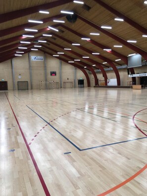 An indoor sports hall with a wooden floor, multiple sports courts, and a high ceiling with linear lighting.