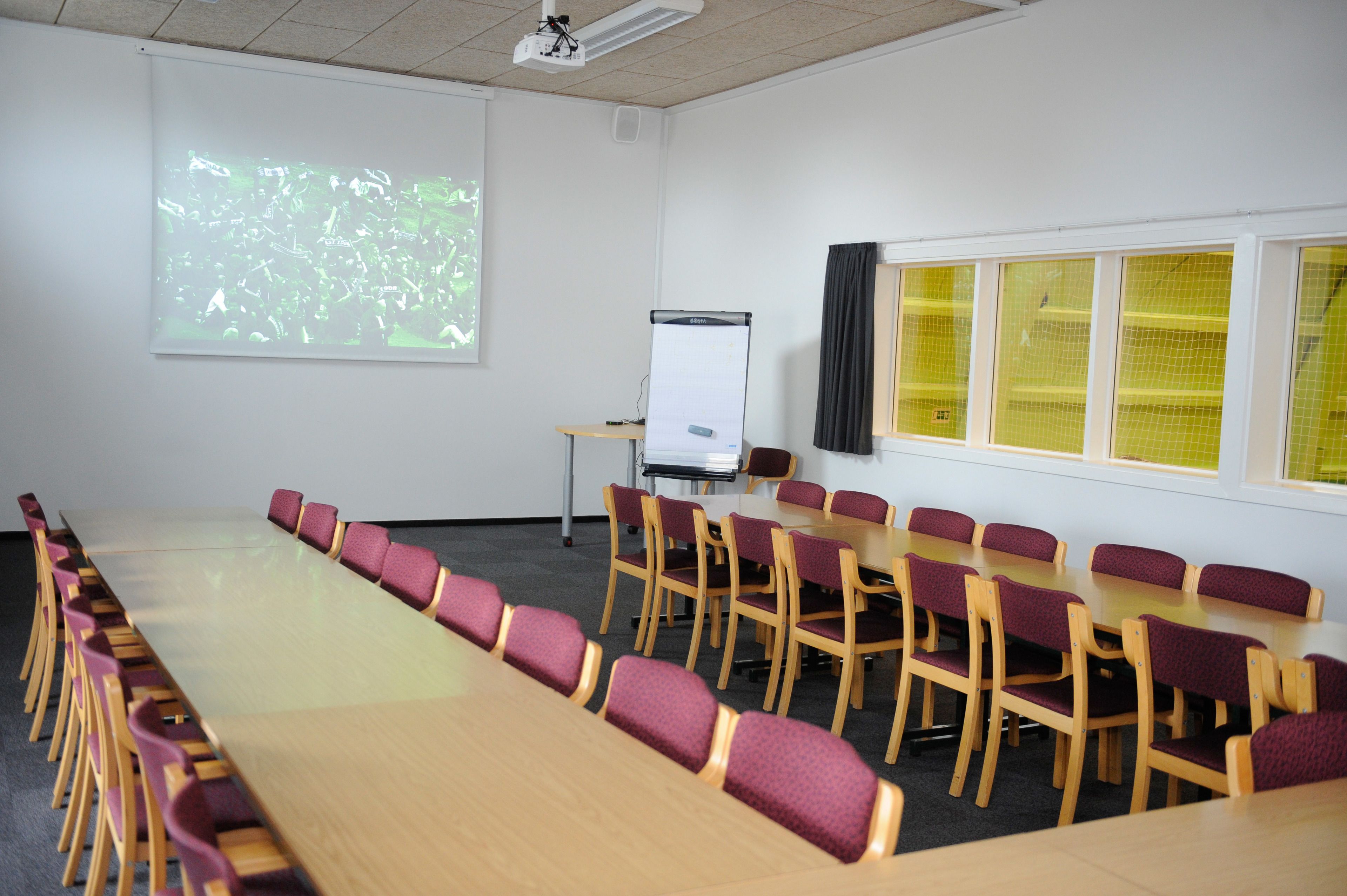 A conference room with a long table and chairs, a whiteboard, and a projector screen.