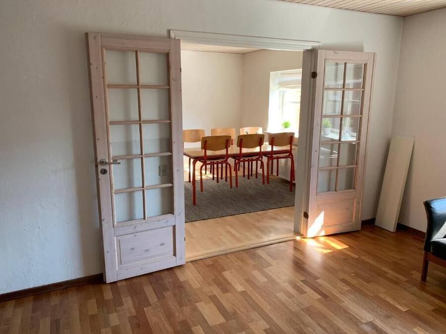 Una habitación con piso de madera, una mesa de comedor con sillas y una puerta que conduce a otra habitación.
