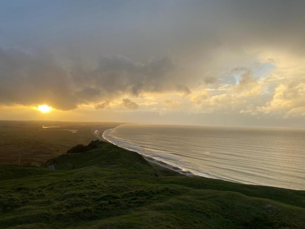 A coastal landscape with a view of the ocean and a grassy hill.