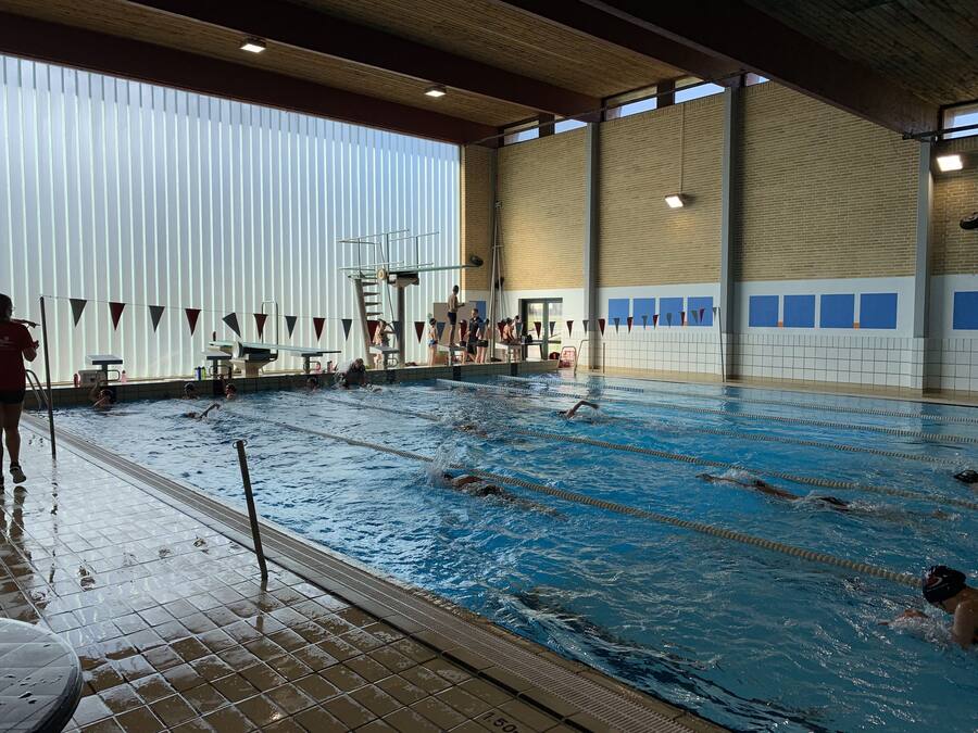 Una piscina interior con múltiples carriles, un trampolín y una zona para espectadores.