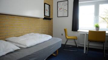 A room with a bed, a chair, a desk, a window, and two wall-mounted pictures.