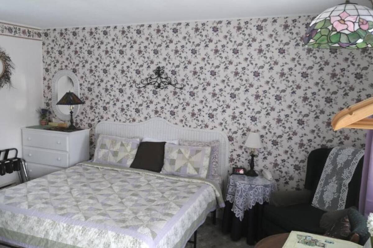 A bedroom with a bed, dresser, nightstand, and a floral-patterned wallpaper.