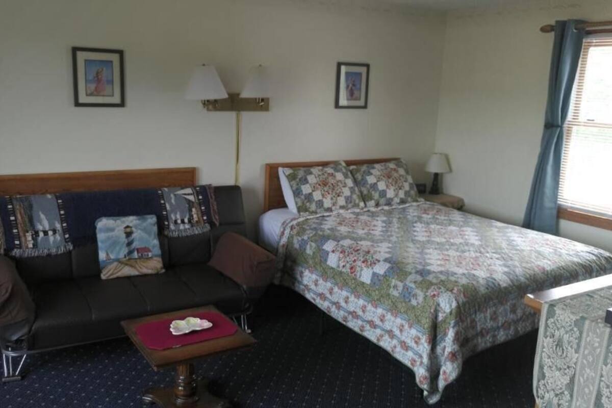 A hotel room with a bed, a sofa, a small table, and a lamp.