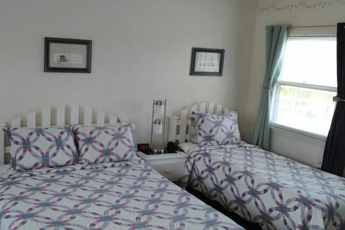 A bedroom with two beds, each with a patterned bedspread, a bedside table with a lamp, and a framed picture on the wall.