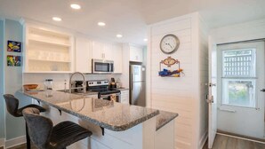 A modern kitchen with white cabinetry, a granite countertop, and a built-in microwave.