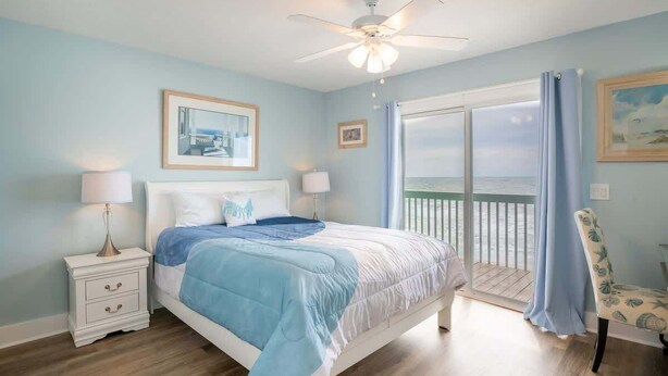 A bedroom with a bed, nightstands, a ceiling fan, and a view of the ocean through a sliding door.