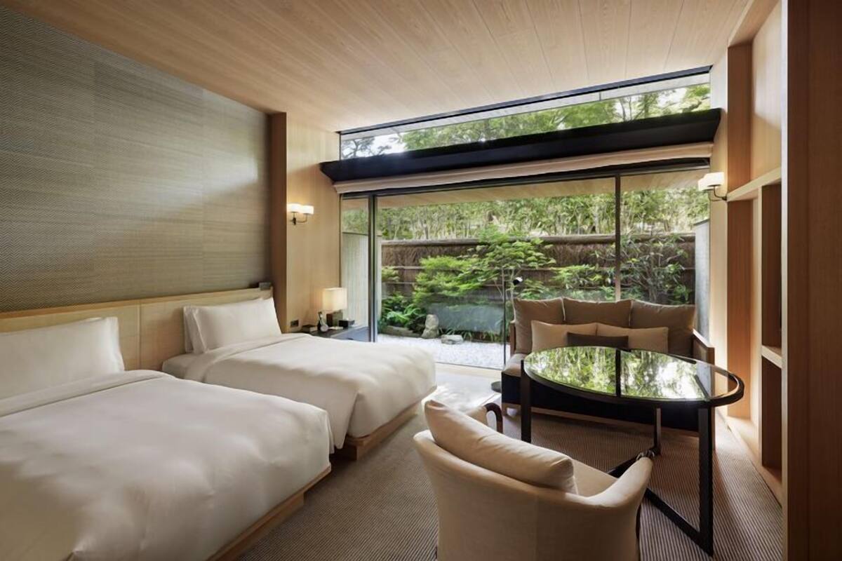 Ein Hotelzimmer mit zwei Betten, einem Glastisch und Blick auf Grünfläche.