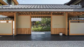 A traditional Japanese-style building with a tiled roof and wooden beams, a stone-tiled entrance, and a small garden with rocks and greenery.