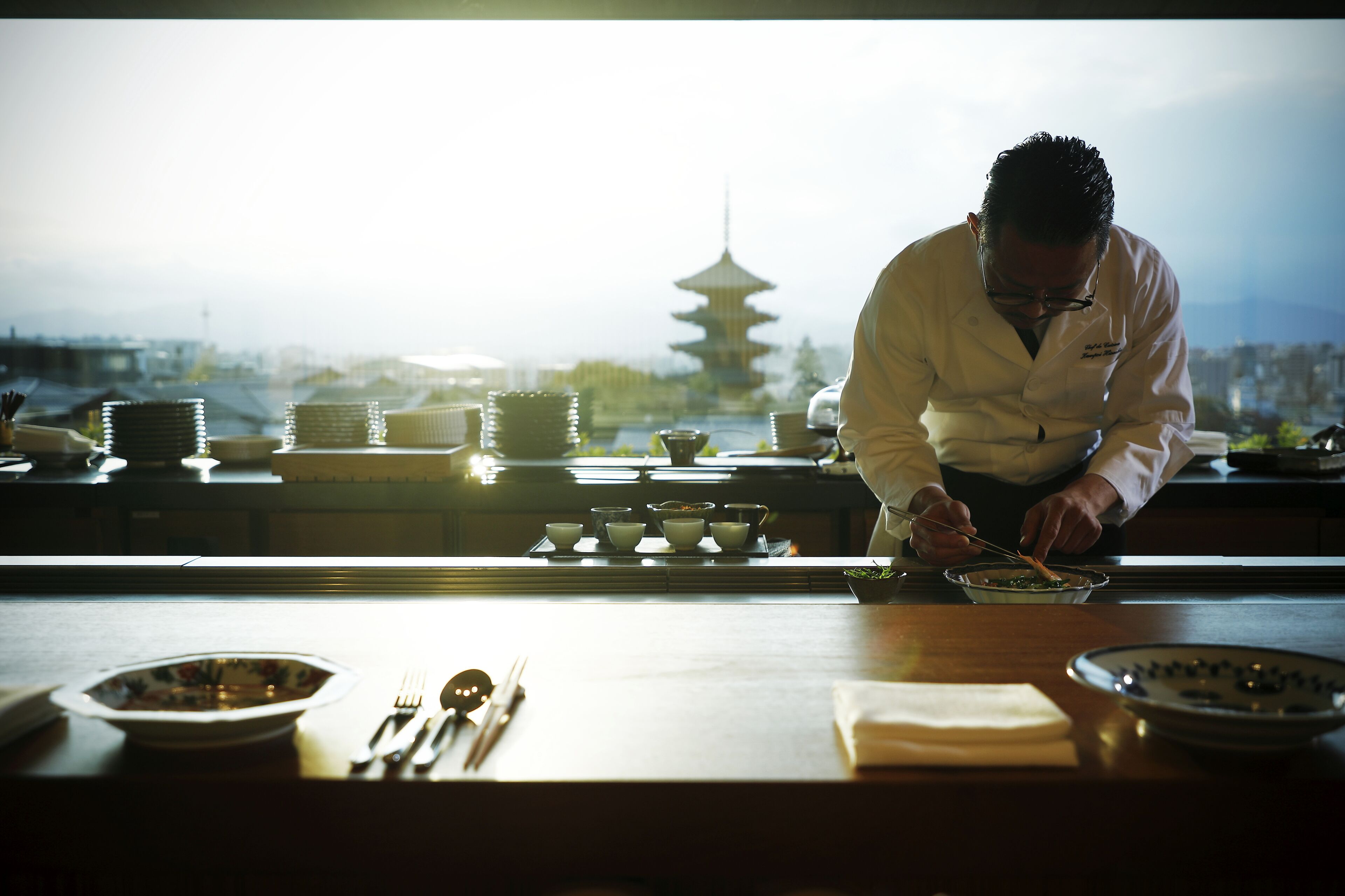 Un chef prepara comida en una mesa con vista a una pagoda al fondo.