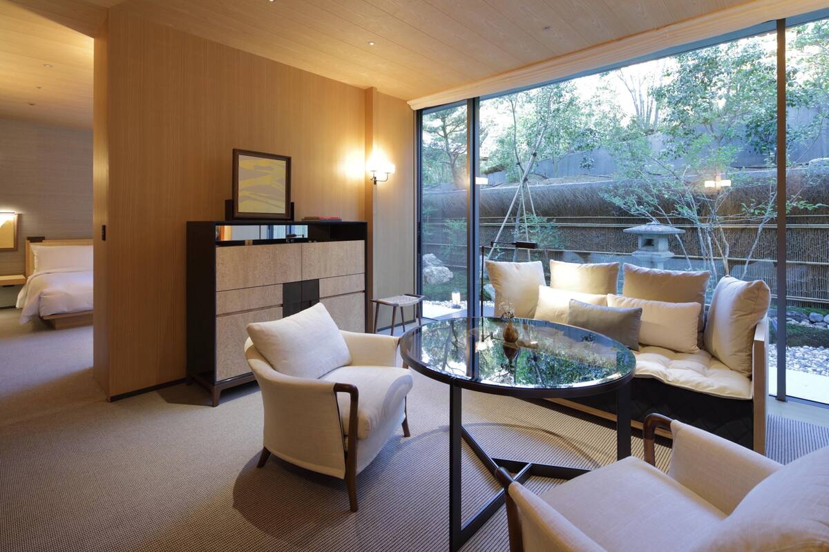 Ein modernes Hotelzimmer mit einem großen Glasfenster, einem runden Glastisch und einer Couch mit Kissen.