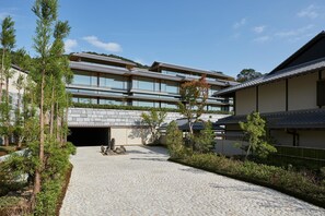 A traditional Japanese building with a modern extension, featuring a stone-paved courtyard and surrounding greenery.