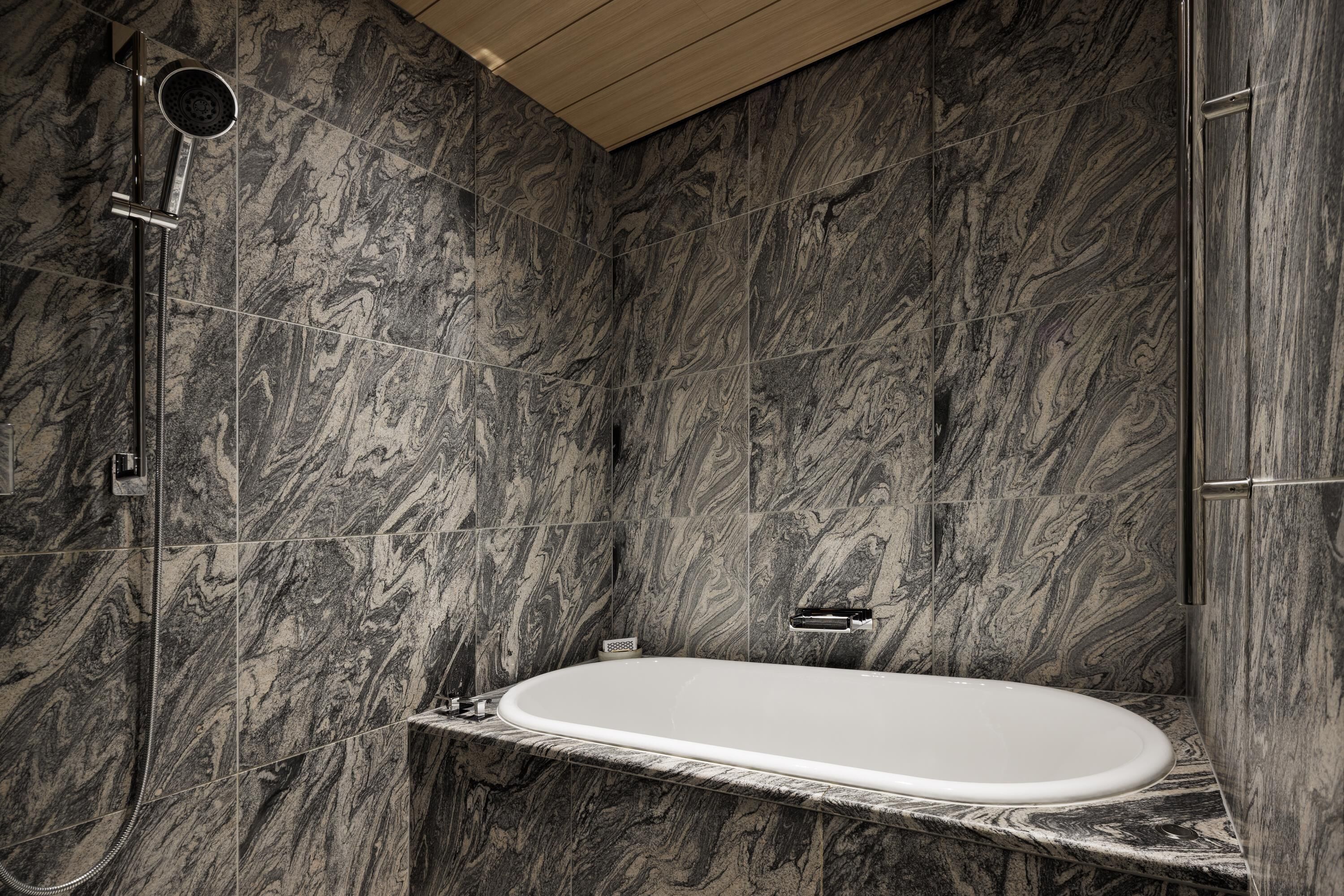 Une salle de bain moderne avec une baignoire sur pieds, des murs en marbre et une pomme de douche.