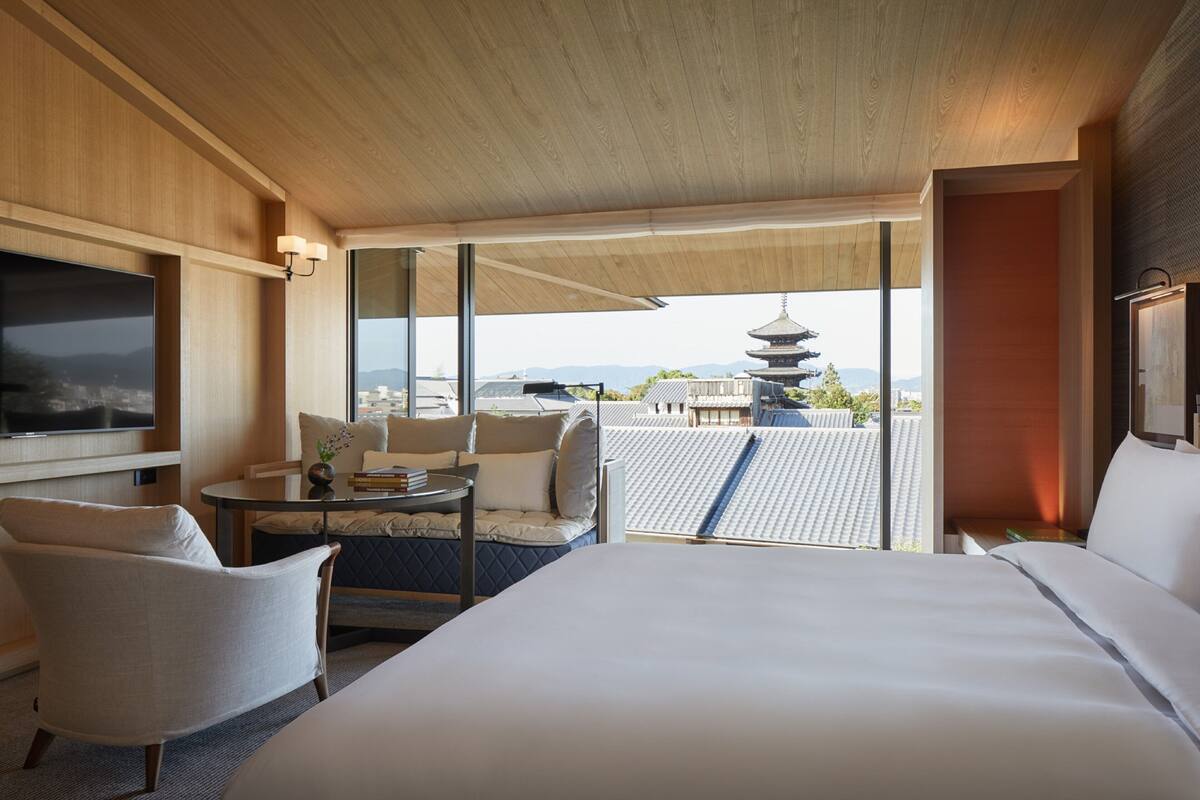 Ein Hotelzimmer mit einem großen Bett, einer Sitzecke mit Tisch und Blick auf eine Pagode durch große Fenster.