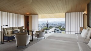 Une chambre d’hôtel avec un grand lit, un canapé, un fauteuil et une vue sur le paysage urbain, qui comprend une pagode.