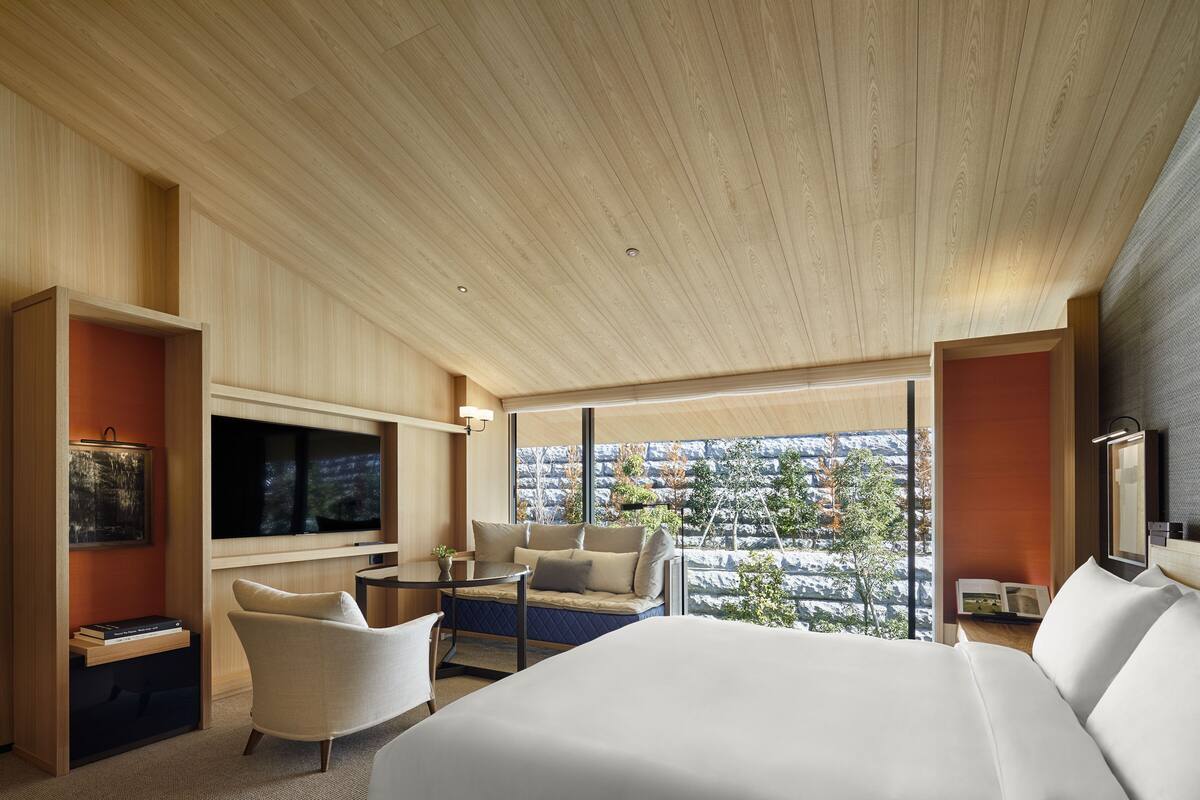 Ein modernes Hotelzimmer mit einem großen Bett, einer Sitzecke mit Sofa und Sesseln, einem Flachbildfernseher und Blick auf eine verschneite Landschaft durch große Fenster.