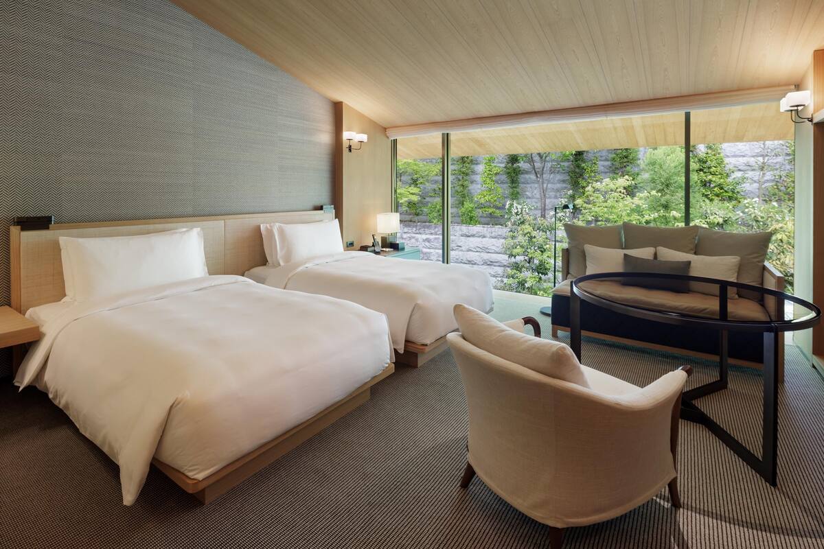 Ein modernes Hotelzimmer mit zwei Betten, einem runden Tisch und einem Sessel.
