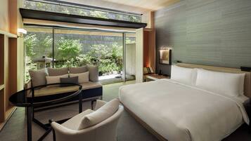 Une chambre d’hôtel moderne dotée d’un grand lit, d’un canapé, d’une petite table et offrant une vue sur un jardin grâce à de grandes fenêtres.