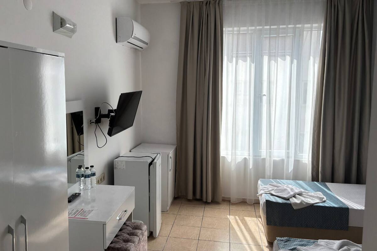 A hotel room with a bed, a desk with a computer, a chair, and a window with curtains.