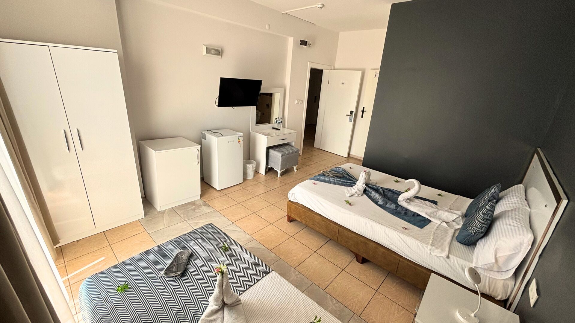 A compact hotel room with a bed, a desk, a wardrobe, and a small kitchenette.