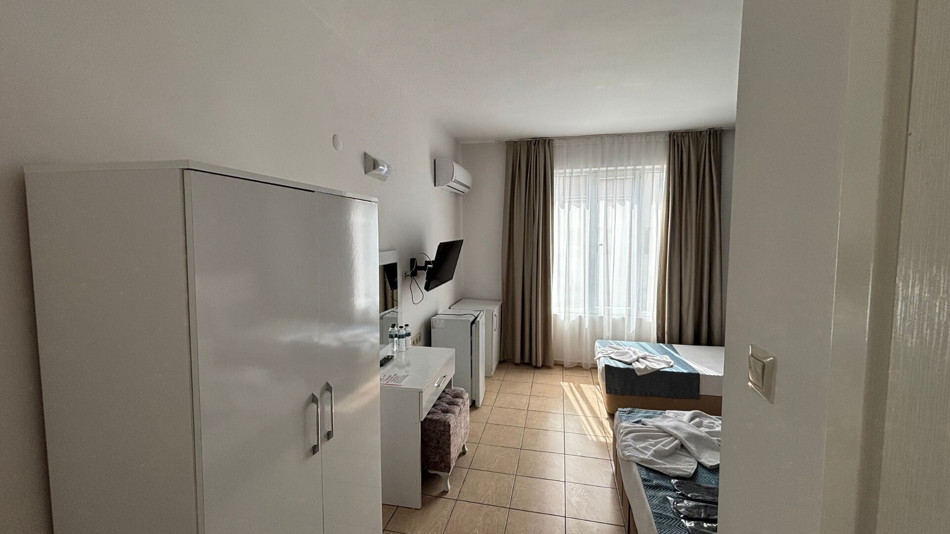 Een compacte hotelkamer met kitchenette, een bed, bureau en raam met gordijnen.