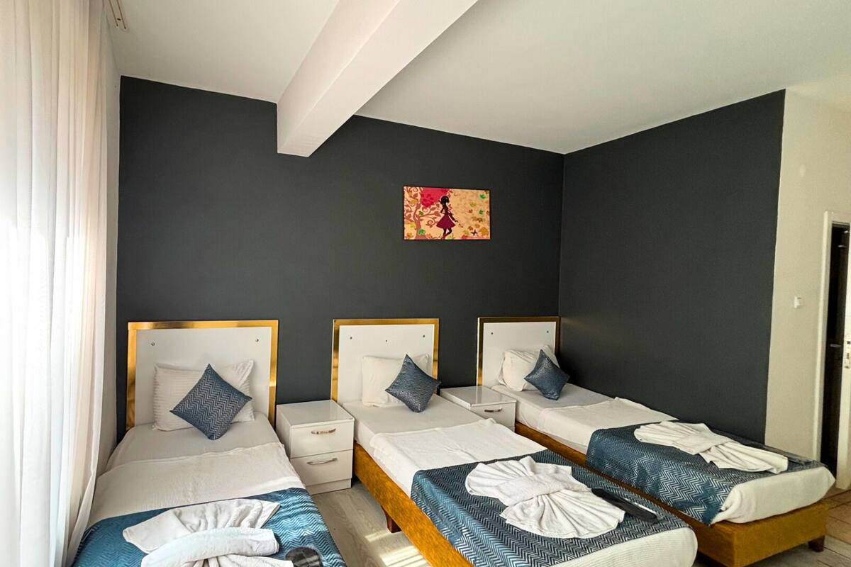 A hotel room with three single beds, each with a wooden headboard and a white nightstand. There is a small white drawer under each bed.