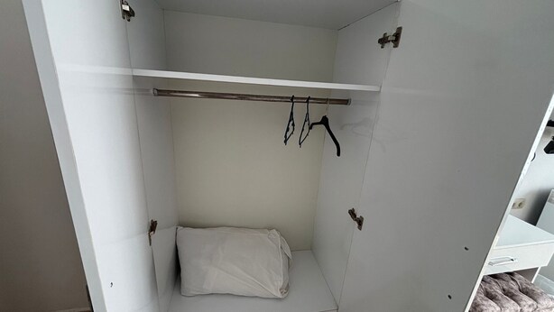 A small, white, walk-in closet with a single hanging rod and a bench. - Moonbow Beach Hotel (Alanya)
