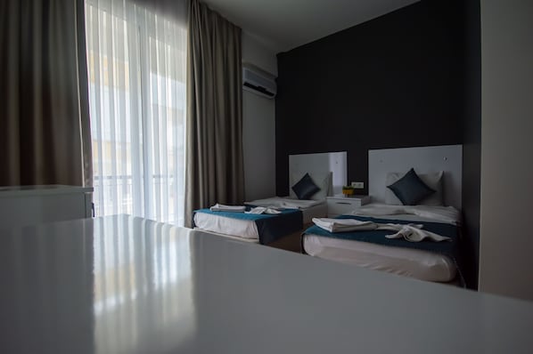 Habitación de hotel con dos camas, un ventanal con cortinas, un equipo de aire acondicionado y una mesa blanca.