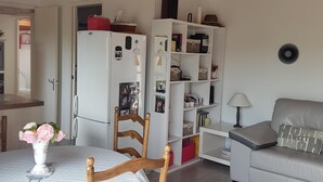 Un espacio habitable compacto con una mesa de comedor, sillas, un sofá, una estantería blanca y un refrigerador.