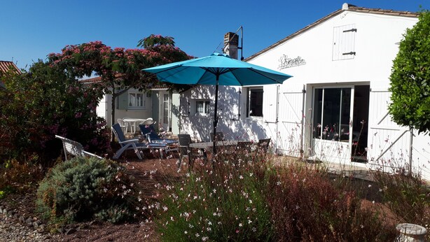 Un edificio blanco con una sombrilla azul, mesas al aire libre y plantas con flores.
