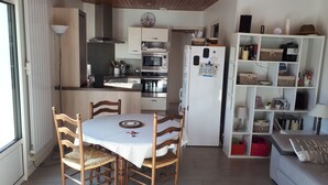 Una cocina funcional con electrodomésticos modernos, un comedor con mesa y sillas, y una sala de estar con sofá y estanterías.