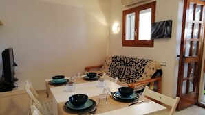 Un comedor con una mesa dispuesta para dos personas, un sofá y una televisión.