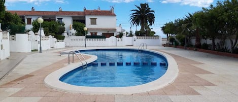 A swimming pool with a tiled deck, surrounded by white walls and a palm tree.