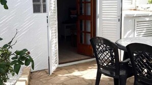 Un patio con piso de piedra, una mesa con sillas y una puerta entreabierta que da a un espacio interior.