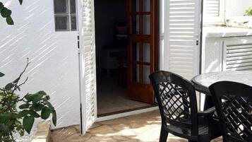 Een patio met stenen vloer, een tafel met stoelen en een gedeeltelijk open deur naar een binnenruimte.