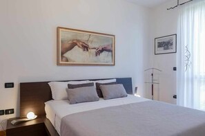 Camera d'albergo con un letto grande, un comodino con una lampada, un quadro appeso alla parete e una finestra con tende.