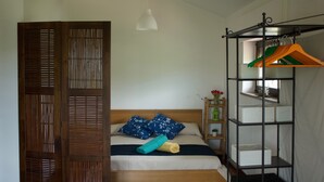 Een slaapkamer met een bed, een houten garderobe, een kledingrek en een nachtkastje met een bloemenvaas.