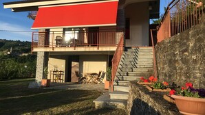 Een huis met twee verdiepingen, voorzien van een rood luifel, een balkon met hekwerk en een trap naar de bovenverdieping.
